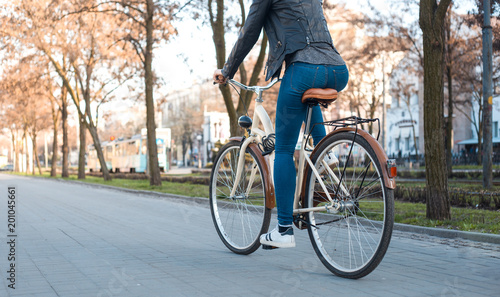 A girl in a leather jacket and jeans rides a bicycle along the avenue in the spring