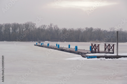 Winter scenery. Timber jetty in frozen river on a foggy winter day.
