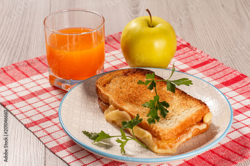 Toast with butter and cheese on white plate, apple and glass of orange juice.
