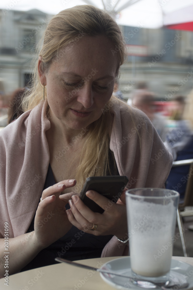 Mujer escribiendo en su teléfono sentada en la terraza de una cafetería. Sobre la mesa su vaso de café. Mujer escribiendo en su teléfono sentada en la terraza de una cafetería. Sobre la mesa su vaso de café.