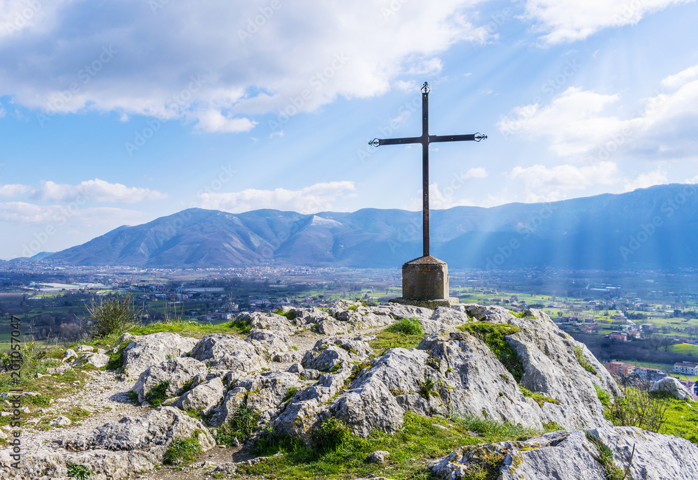 A steel cross on top of the mountain and rays of the sun. Beautiful landscape.