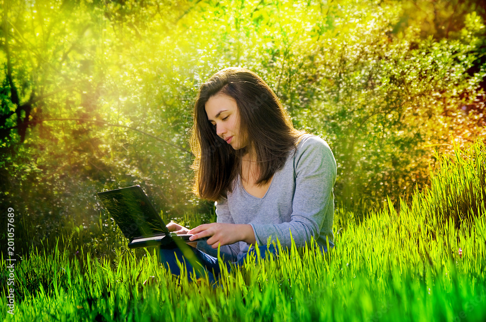 young beautiful happy girl sits in park in green grass with laptop young beautiful happy girl sits in park in green grass with laptop