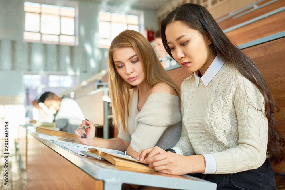Two beautiful girls studying notes sitting at desk in lecture hall of modern college, copy space Two beautiful girls studying notes sitting at desk in lecture hall of modern college, copy space