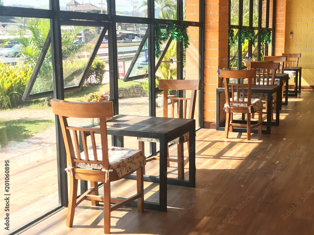 Classic wooden table and chair with cushion in coffee shop or restaurant over yellow brick wall and sun light