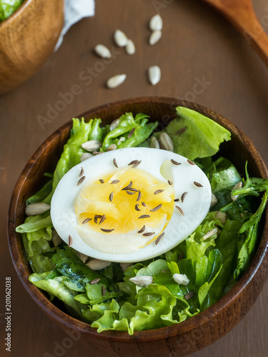 Salad of lettuce leaves and eggs in wooden bowls seeds cumin loaves Dark background