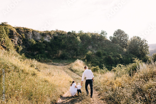 Walk beautiful young family in white clothes with a young son blond in mountainous areas with tall grass at sunset. Mother keeps son in her arms, hugging. family - this is happiness © Oleksandr