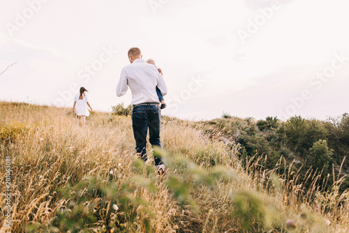 Walk beautiful young family in white clothes with a young son blond in mountainous areas with tall grass at sunset. Mother keeps son in his arms, hugging. family - this is happiness © Oleksandr