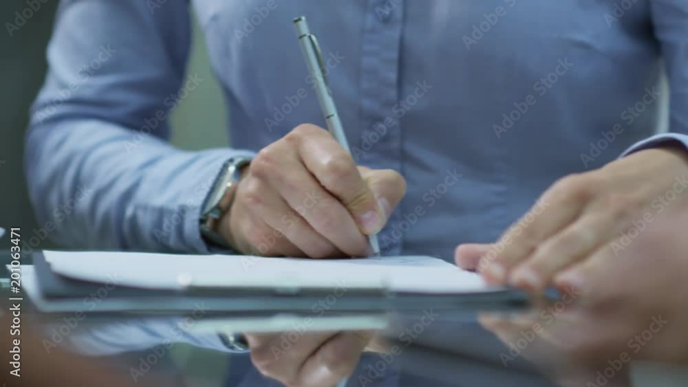 Tracking shot of hands of unrecognizable businessman signing agreement at meeting