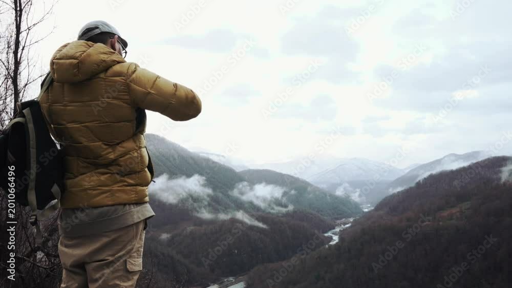 Photo artist is shooting landscape with mountains and river in a fall morning. He is standing on hill and looking in an camera lens, back view Photo artist is shooting landscape with mountains and river in a fall morning. He is standing on hill and looking in an camera lens, back view