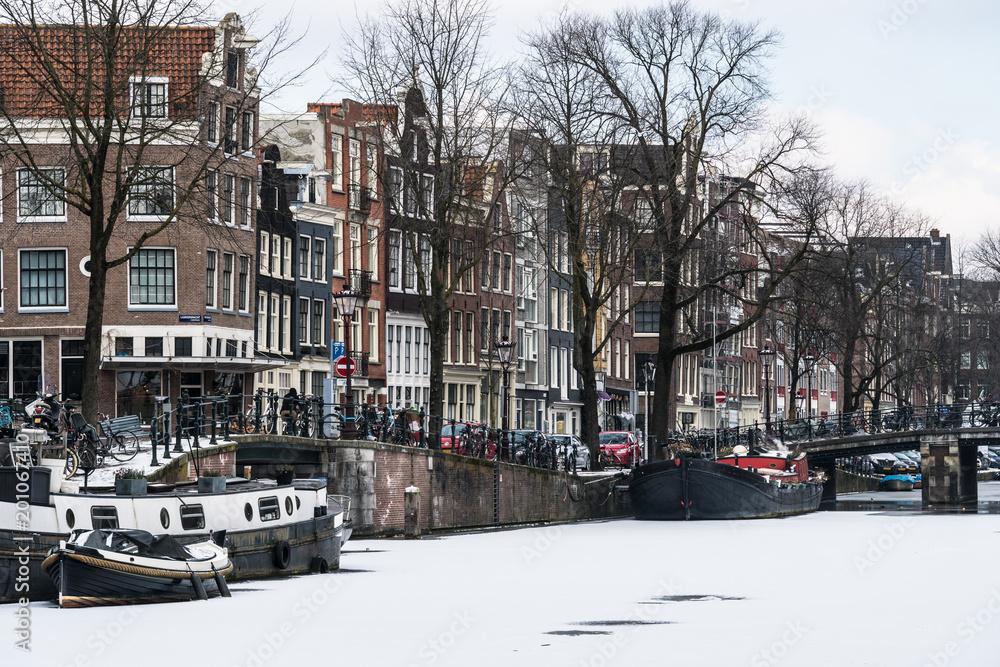 Stunning view of Amsterdam canals and house boat frozen with snow during the cold wave in February 2018 on a very cold winter day.