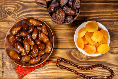 Dried apricots and dates fruit with wooden rosary on wooden table. Top view