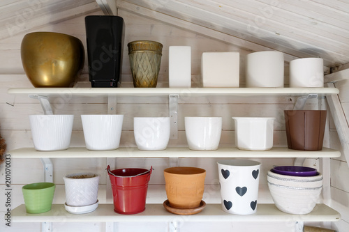 Many pots in different shapes and sizes lined up on shelves in a garden shed.