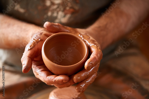 Photos Close-up hands of a male potter in apron molds bowl from clay, selective focus