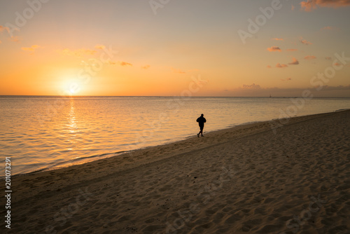 One silhouette running alone on the beach at sunset in Mauritius.