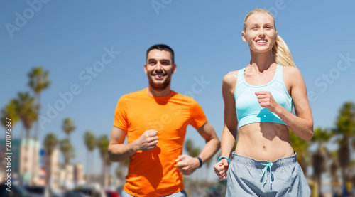 fitness, sport and healthy lifestyle concept - smiling couple jogging at summer over venice beach background in california