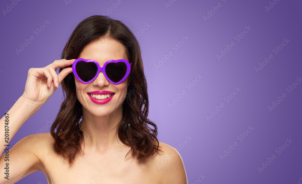 valentines day, beauty and people concept - happy smiling young woman with pink lipstick and heart shaped sunglasses over ultra violet background valentines day, beauty and people concept - happy smiling young woman with pink lipstick and heart shaped sunglasses over ultra violet background
