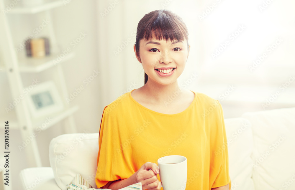 people, drinks and leisure concept - happy asian woman sitting on sofa and drinking tea from cup or mug at home people, drinks and leisure concept - happy asian woman sitting on sofa and drinking tea from cup or mug at home
