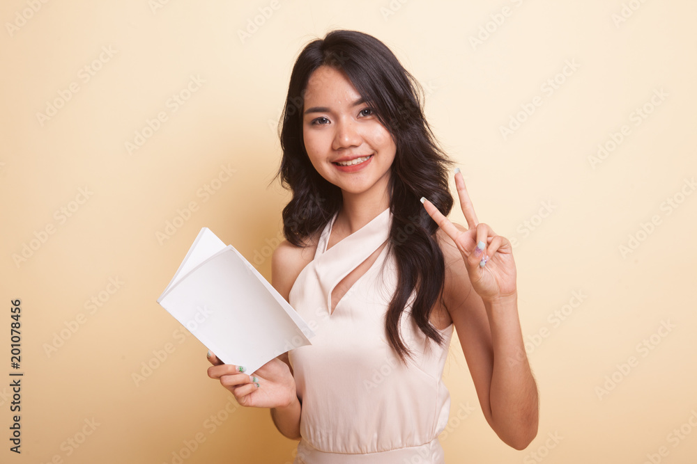 Young Asian woman show victor sign with a book. Young Asian woman show victor sign with a book.
