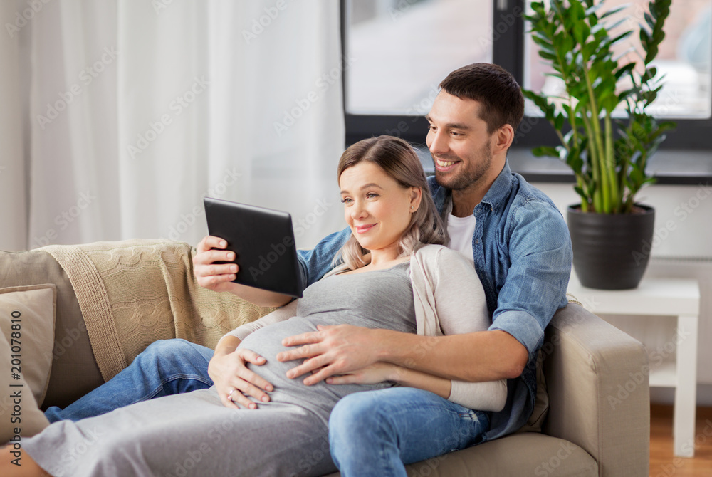 pregnancy, technology and people concept - happy man and his pregnant wife with tablet pc computer at home pregnancy, technology and people concept - happy man and his pregnant wife with tablet pc computer at home
