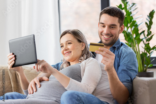 online shopping, pregnancy and technology concept - happy man and his pregnant wife with tablet pc computer and credit card at home