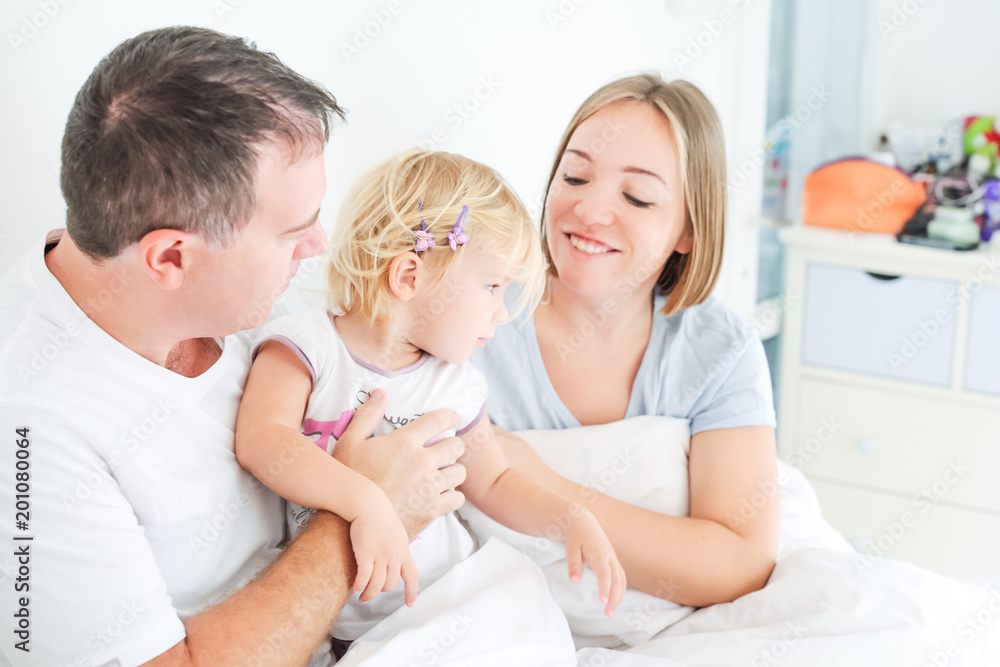 Happy and loving family morning concept. Cheerful parents in sleepwear having fun with their daughter on the bed. Family spending free time together at home.Soft selective focus. Space for text.