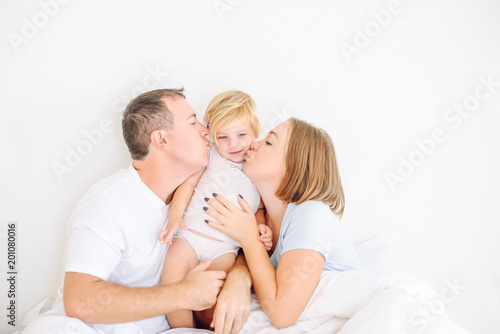 Happy and loving family morning concept. Cheerful parents in sleepwear having fun with their daughter on the bed. Family spending free time together at home.Soft selective focus. Space for text.