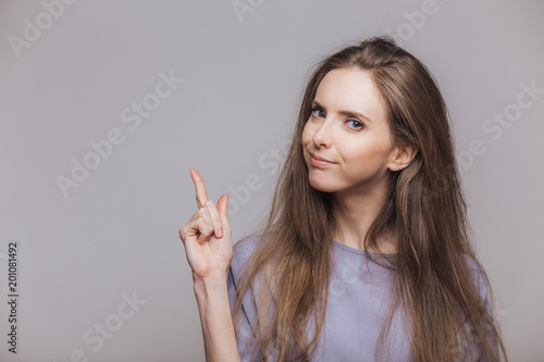 Look there! Adorable brunette female model with attractive look, indicates with fore finger at blank copy space, shows place fot your advertising content or promotional text. Advertisment concept