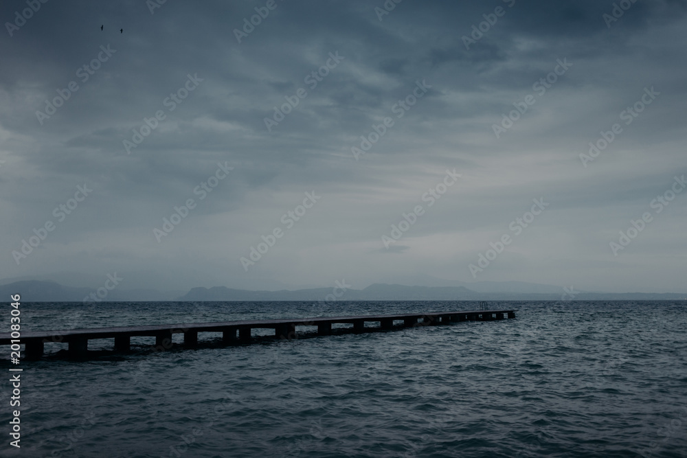 View of wooden pier across seashore and blue sky with white clouds, turquois water. Wonderful perspective view of ocean. Calm atmosphere. Outdoor shot