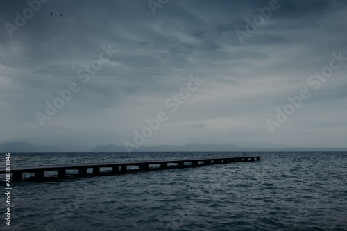 View of wooden pier across seashore and blue sky with white clouds, turquois water. Wonderful perspective view of ocean. Calm atmosphere. Outdoor shot