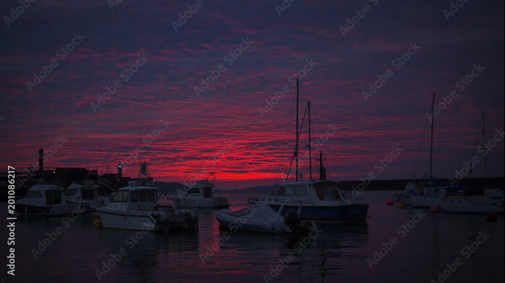 Deep red sunrise over sailing boats and fishing boatsin harbour at St Peters Port Guernsey