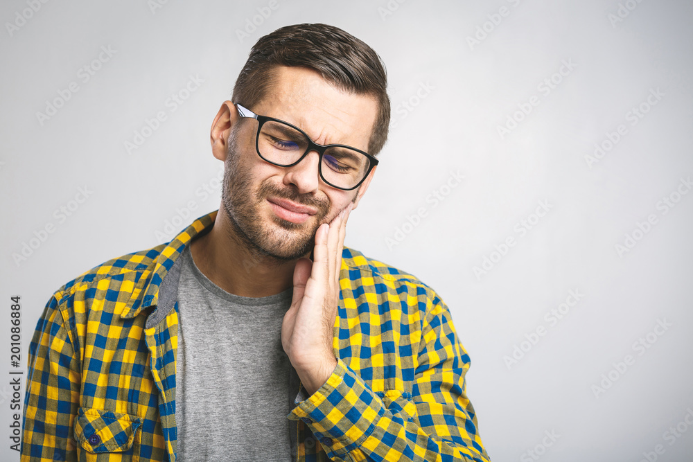 Toothache. Frustrated young man touching his cheek and keeping eyes closed while sitting on the couch at home Toothache. Frustrated young man touching his cheek and keeping eyes closed while sitting on the couch at home