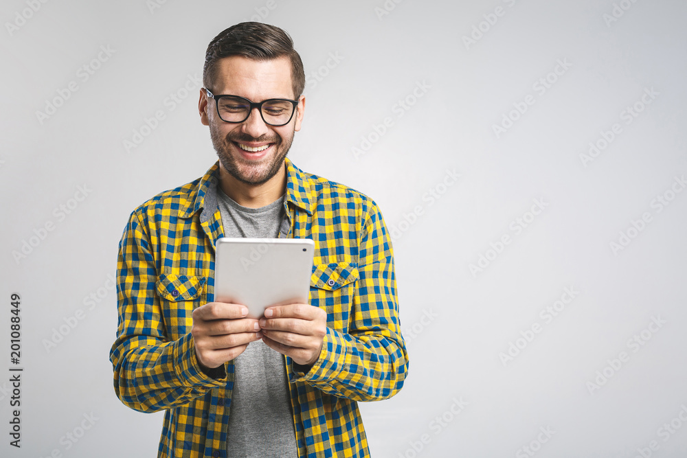 Happy young man in plaid shirt standing and using tablet over grey background Happy young man in plaid shirt standing and using tablet over grey background