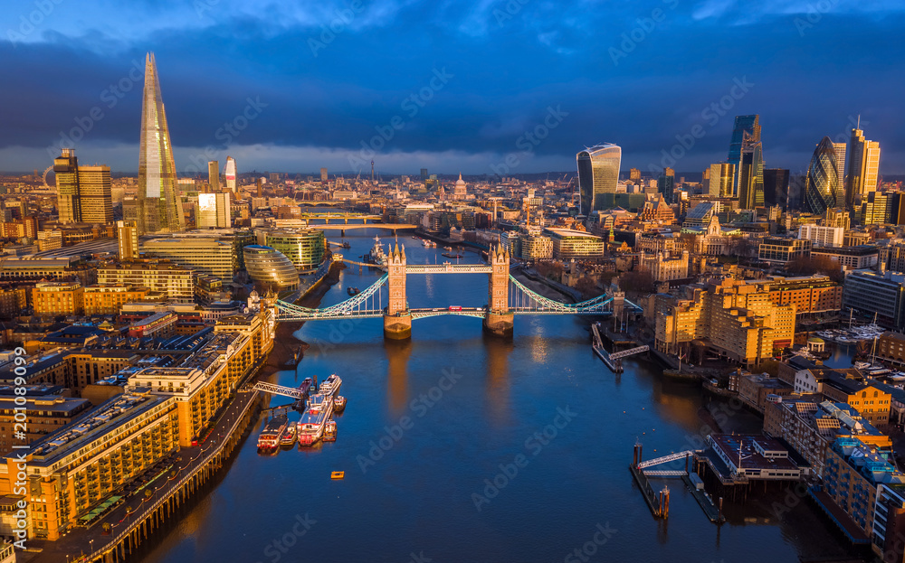 London, England - Aerial skyline view of London including iconic Tower Bridge with red double-decker bus, Tower of London, skyscrapers of Bank District at golden hour early in the morning 
