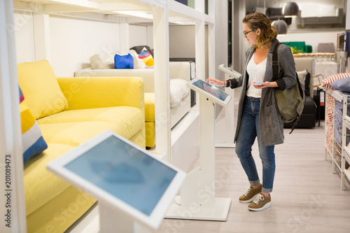 Woman with phone configuring furniture at the self-service device in the store photo