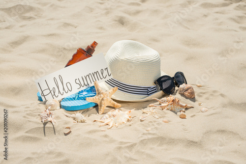 Hat on the beach, sunglasses, sea shells and a star and an inscription hi summer. On white sand photo