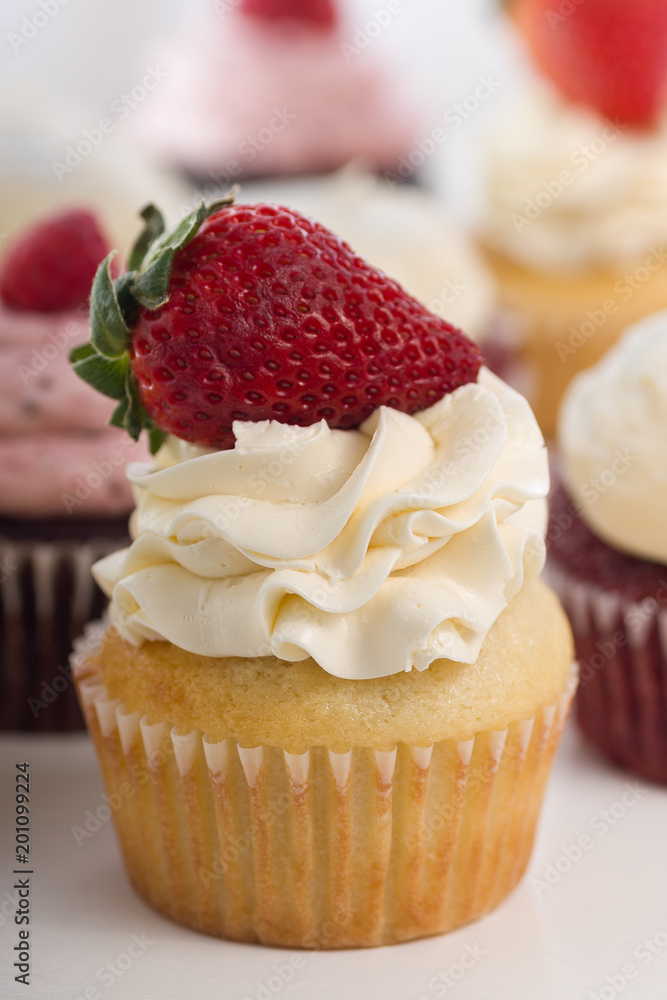 Vanilla Cupcake With A Strawberry Topper. Assortment Of Cupcakes In Background.