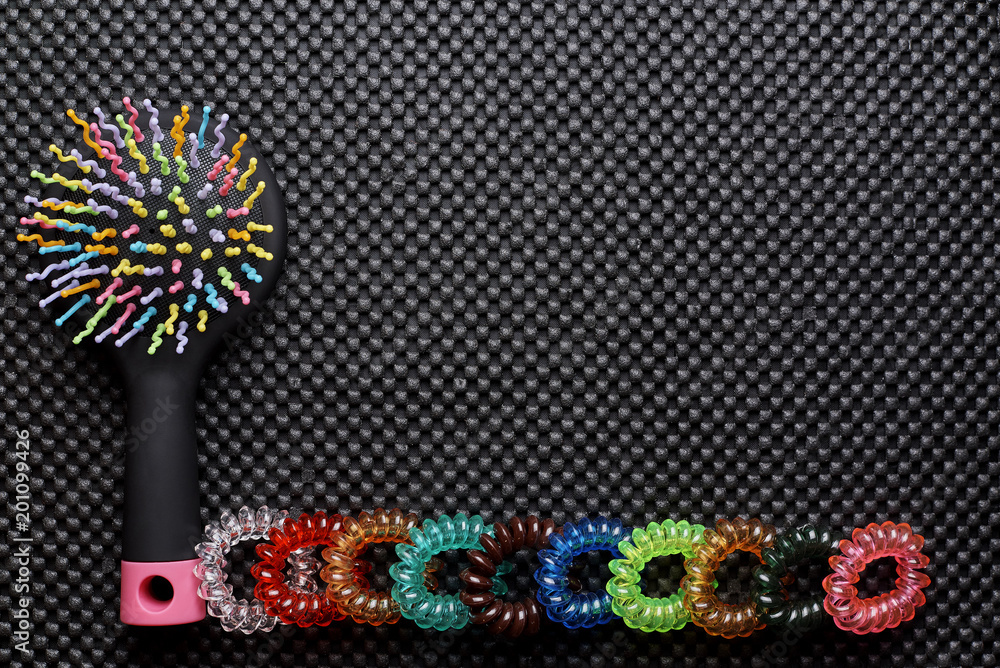 Bright multicolored comb and a row of colored rubber bands on a black background. Copy space.