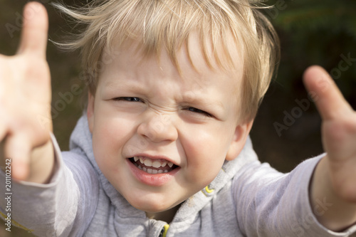 Sad crying toddler pulls his hands up. Close up portrait of baby boy asking for pick up