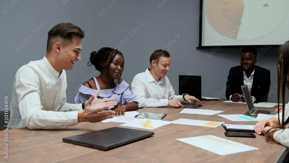A group of creative multi-ethnic managers disassemble at the meeting of the board of directors in the conference hall the graphs of profit for the last year in the firm. The boss of an African A group of creative multi-ethnic managers disassemble at the meeting of the board of directors in the conference hall the graphs of profit for the last year in the firm. The boss of an African