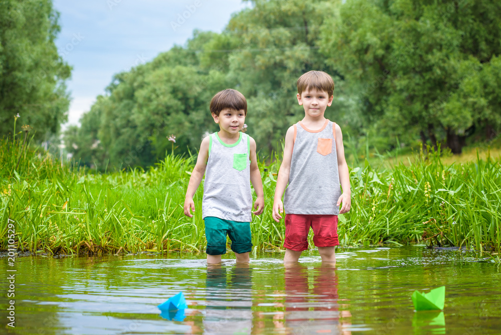 Two little brothers playing with paper boats by a river on warm and sunny summer day. Two little brothers playing with paper boats by a river on warm and sunny summer day.