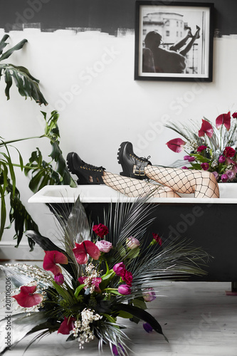Fototapeta Naklejka Na Ścianę i Meble -  Sexy slim woman's legs in mesh pantyhose and black boots in black retro bath in bathroom with flower compositions