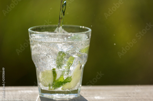 a glass with ice cubes, with lime and with mint, soda water from the bottle, in the open space, sunlight and bokeh
