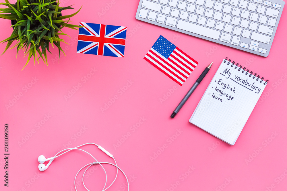 Fototapeta premium Learn english concept. British and american flags, computer keyboard, notebook for new vocabulary on pink background top view copy space