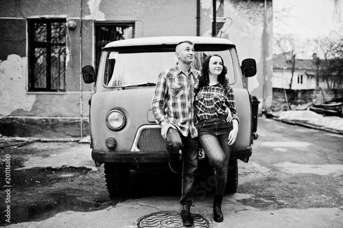 Stylish couple wear on checkered shirt in love together against old minivan.