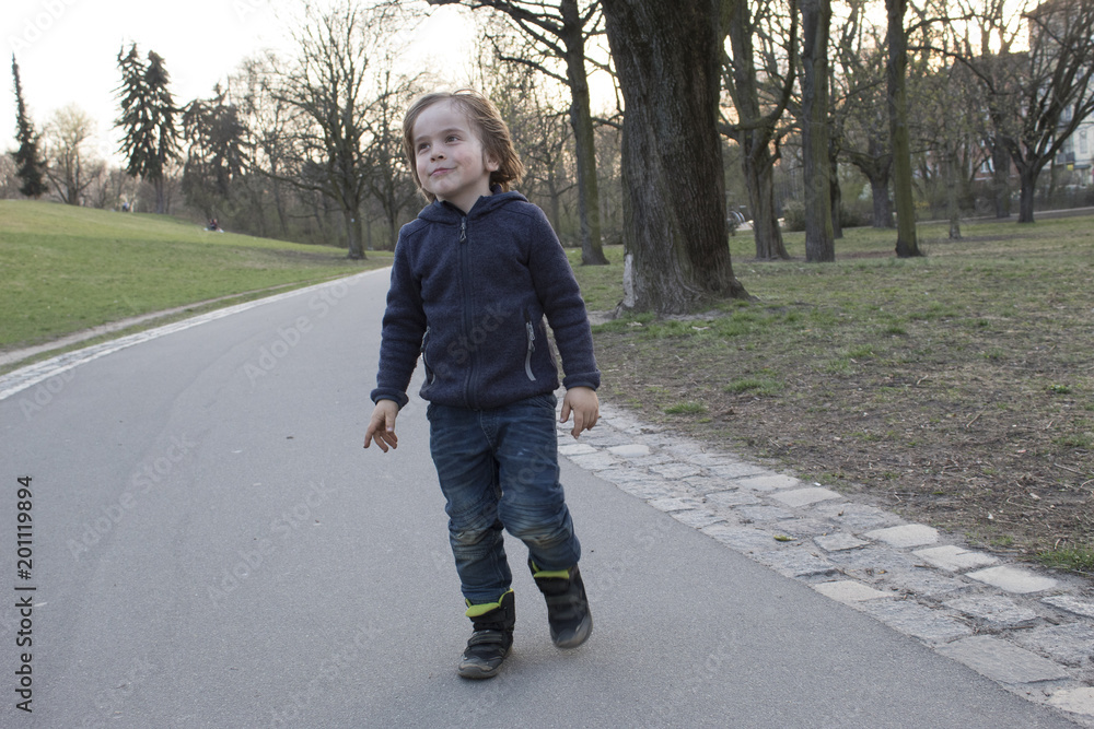 Fototapeta premium Niño ilusionado andando por un parque con árboles. Alemania.