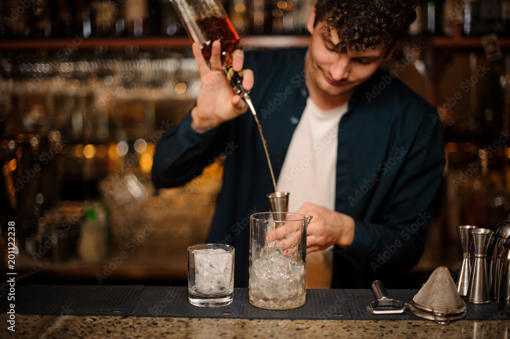 Brunet bartender pouring an alcoholic drink into a measuring cup