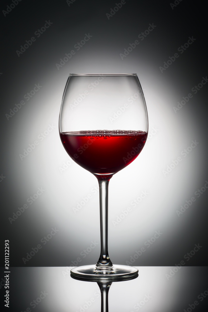 Fototapeta premium Large glass red wine shape of dark from grapes alcoholic beverage on luminous background advertising shot