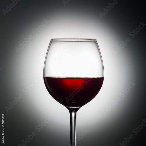 Large glass red wine shape of dark from grapes alcoholic beverage on luminous background advertising shot