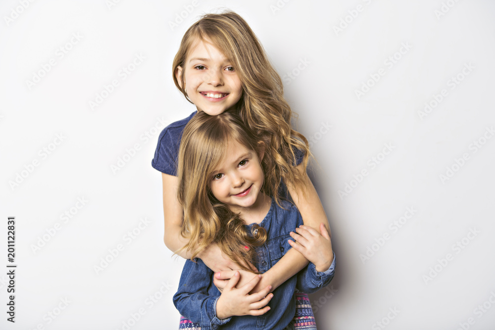 Joyful beautiful child with her sister close to a white wall - obrazy, fototapety, plakaty 