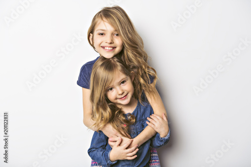 Joyful beautiful child with her sister close to a white wall photo